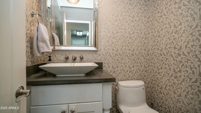 bathroom with vanity, toilet, and wallpapered walls