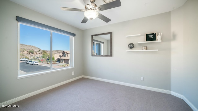 empty room featuring a mountain view, carpet floors, a ceiling fan, and baseboards