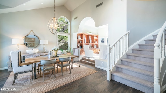 dining area featuring dark wood-style floors, a chandelier, high vaulted ceiling, baseboards, and stairs