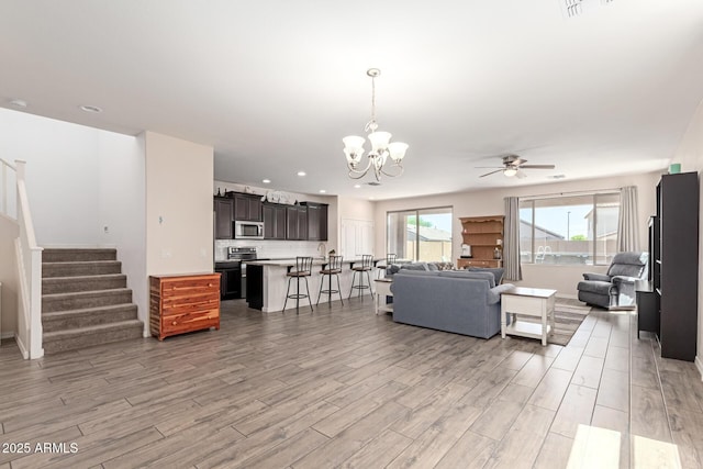 19771 W Woodlands Ave, Buckeye, AZ 85326 - living room with light wood-type flooring, a ceiling fan, a chandelier, stairs, and recessed lighting