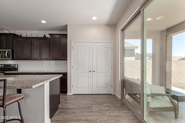19771 W Woodlands Ave, Buckeye, AZ 85326 - kitchen with stainless steel microwave, range, backsplash, dark brown cabinets, and light wood-type flooring