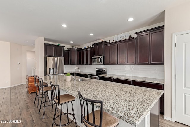 19771 W Woodlands Ave, Buckeye, AZ 85326 - kitchen with appliances with stainless steel finishes, light wood-style flooring, a kitchen breakfast bar, a kitchen island with sink, and tasteful backsplash