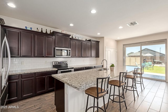19771 W Woodlands Ave, Buckeye, AZ 85326 - kitchen featuring appliances with stainless steel finishes, backsplash, a kitchen breakfast bar, a center island with sink, and light stone countertops