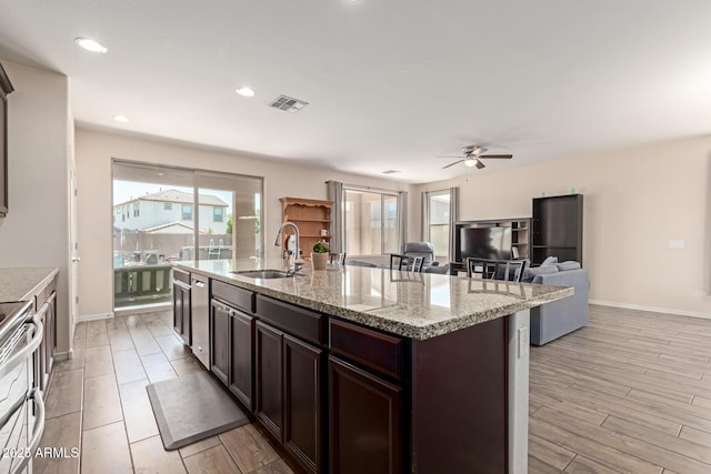 19771 W Woodlands Ave, Buckeye, AZ 85326 - kitchen featuring ceiling fan, dark brown cabinets, appliances with stainless steel finishes, a center island with sink, and light stone countertops