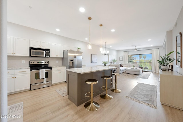 kitchen featuring appliances with stainless steel finishes, a kitchen island, white cabinetry, light wood finished floors, and open floor plan