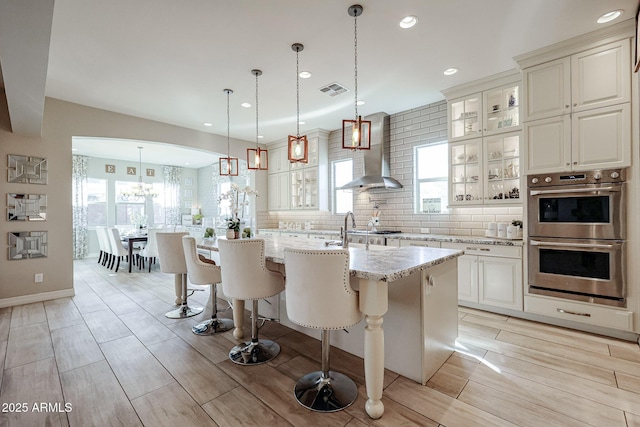 kitchen with wall chimney range hood, tasteful backsplash, visible vents, stainless steel double oven, and recessed lighting