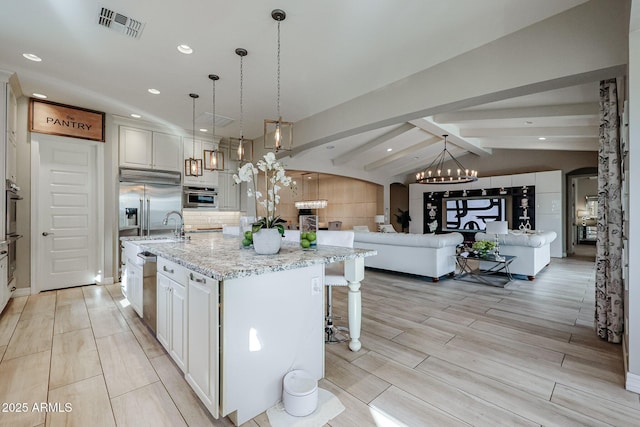 kitchen featuring visible vents, arched walkways, an island with sink, and a sink