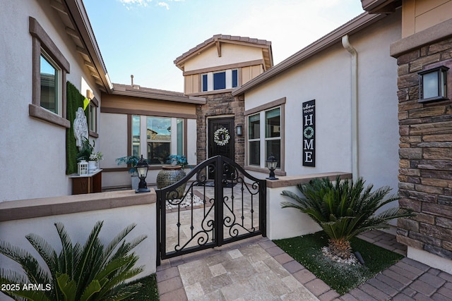 doorway to property featuring a gate, fence, stucco siding, and stone siding