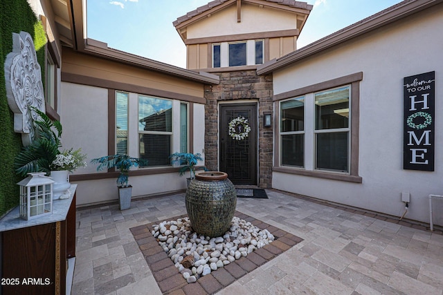 property entrance with stucco siding, a patio area, and stone siding