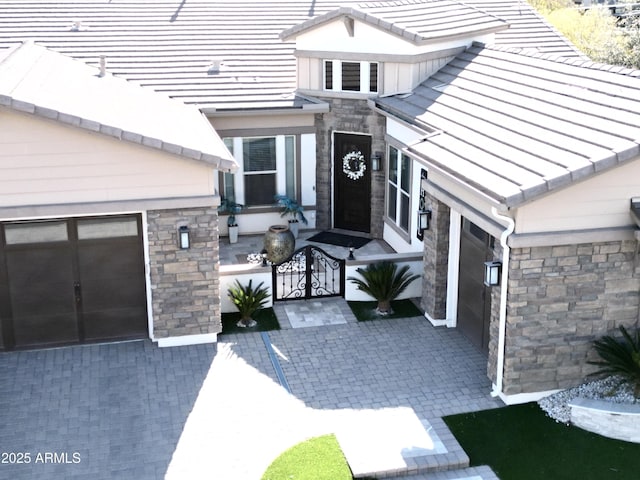 doorway to property featuring a gate, decorative driveway, and stone siding
