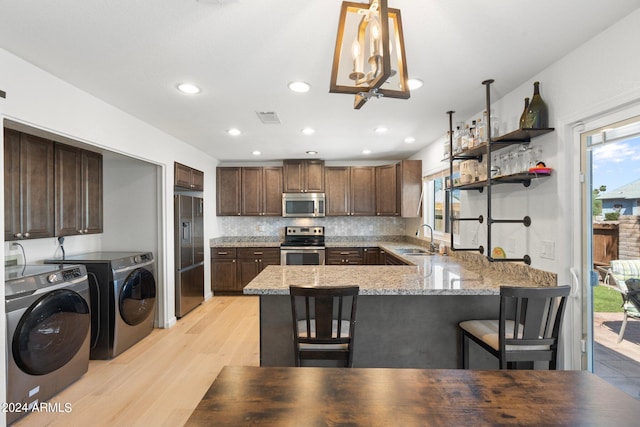 kitchen with a breakfast bar area, appliances with stainless steel finishes, light hardwood / wood-style floors, washer and dryer, and kitchen peninsula