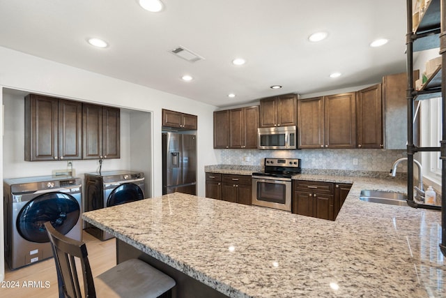 kitchen with light wood-type flooring, appliances with stainless steel finishes, sink, washer and dryer, and kitchen peninsula