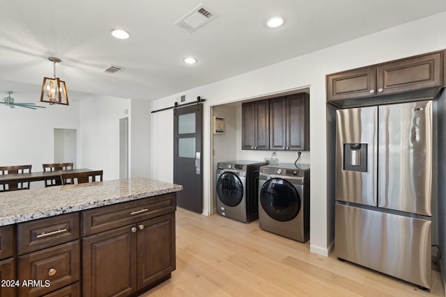 clothes washing area with a barn door, ceiling fan, washer and clothes dryer, and light hardwood / wood-style flooring