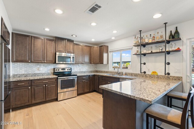 kitchen with light stone countertops, light hardwood / wood-style flooring, a kitchen bar, stainless steel appliances, and sink