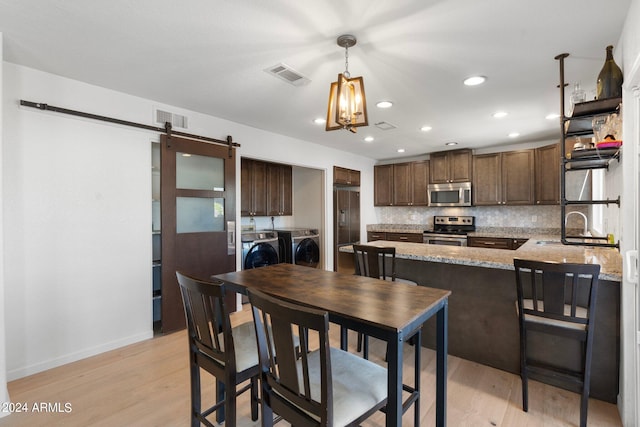 kitchen featuring a barn door, appliances with stainless steel finishes, light hardwood / wood-style flooring, and washing machine and dryer