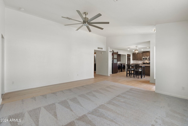 unfurnished room with ceiling fan with notable chandelier, a barn door, and light hardwood / wood-style floors