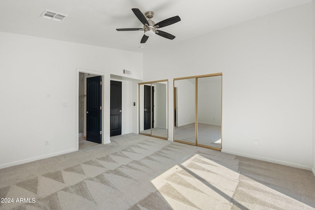 unfurnished bedroom with light colored carpet, vaulted ceiling, multiple closets, and ceiling fan