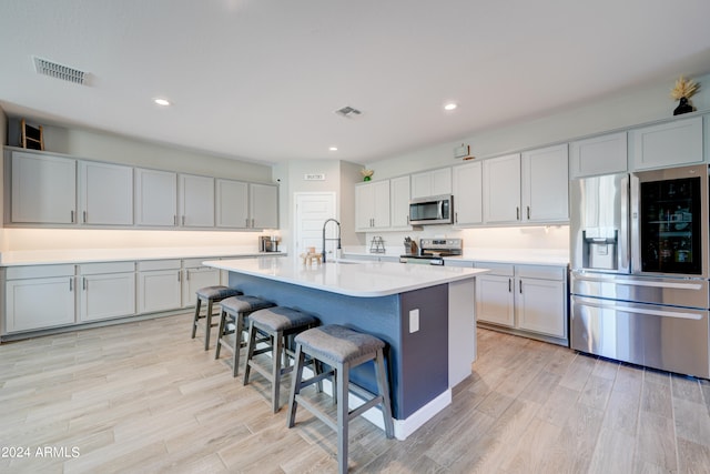 kitchen featuring a kitchen island with sink, stainless steel appliances, sink, a kitchen bar, and light wood-type flooring