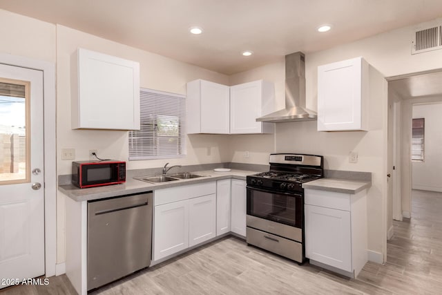 kitchen featuring white cabinets, appliances with stainless steel finishes, a sink, wall chimney exhaust hood, and visible vents