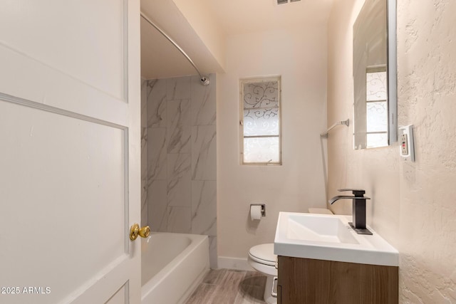 bathroom featuring vanity, a textured wall, toilet, baseboards, and shower / washtub combination