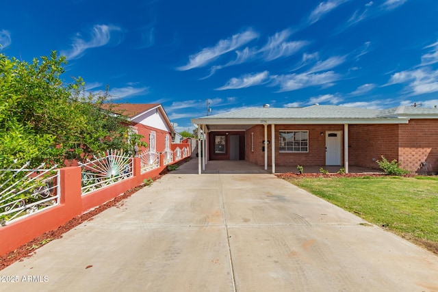 ranch-style home featuring a front lawn, fence, an attached carport, brick siding, and concrete driveway