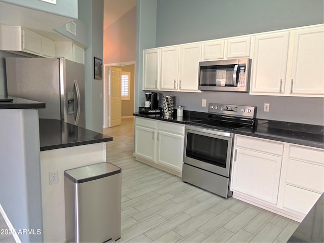 kitchen featuring white cabinetry, appliances with stainless steel finishes, high vaulted ceiling, and light hardwood / wood-style flooring