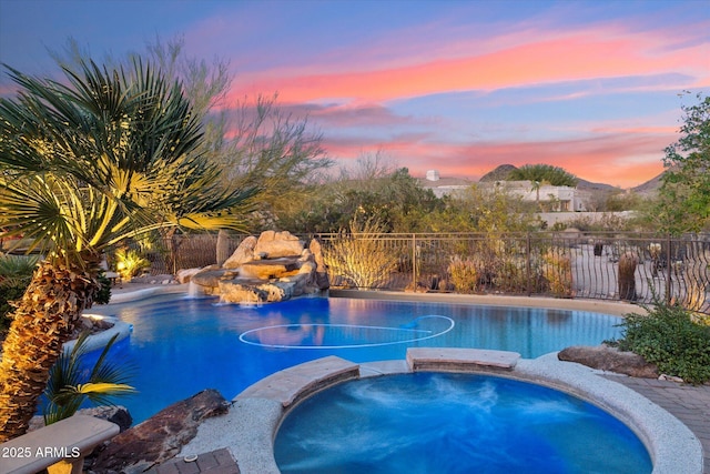 view of swimming pool featuring a pool with connected hot tub, fence, and a mountain view