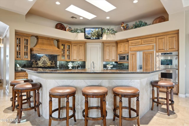 kitchen featuring built in appliances, a skylight, visible vents, dark countertops, and custom range hood