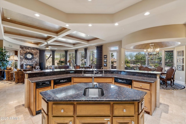 kitchen featuring coffered ceiling, dark stone counters, open floor plan, a kitchen island with sink, and a sink