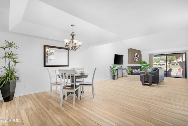 dining area featuring light wood-type flooring, a fireplace with raised hearth, and a chandelier