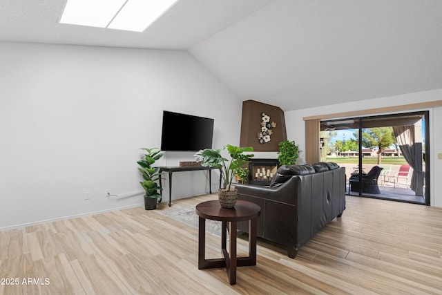 living room featuring light wood-type flooring, a fireplace, and lofted ceiling with skylight