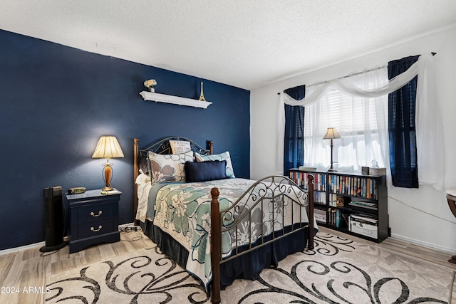 bedroom featuring a textured ceiling, baseboards, and wood finished floors