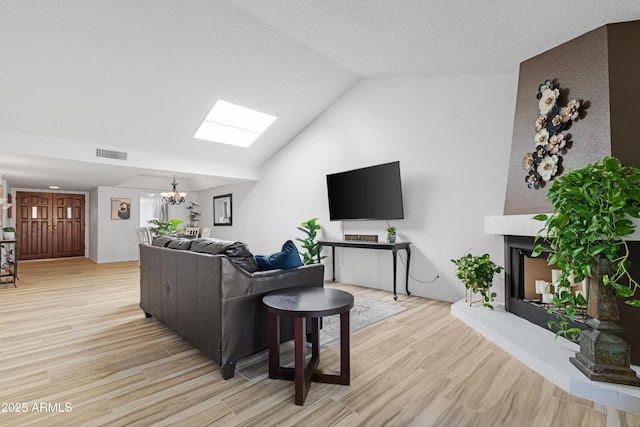 living room featuring vaulted ceiling with skylight, an inviting chandelier, a textured ceiling, light wood-type flooring, and visible vents