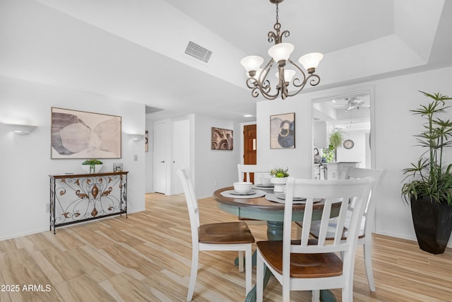 dining room featuring baseboards, light wood-style floors, visible vents, a raised ceiling, and ceiling fan with notable chandelier