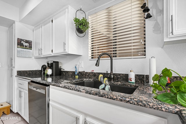 kitchen with dark stone countertops, white cabinetry, a sink, stainless steel dishwasher, and a textured wall