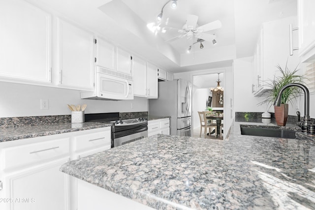 kitchen featuring ceiling fan with notable chandelier, a tray ceiling, white cabinets, a sink, and stainless steel appliances