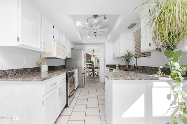 kitchen featuring a raised ceiling, a sink, appliances with stainless steel finishes, a peninsula, and white cabinetry