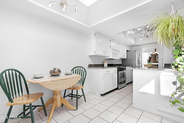 kitchen with a tray ceiling, white microwave, gas range, and white cabinets
