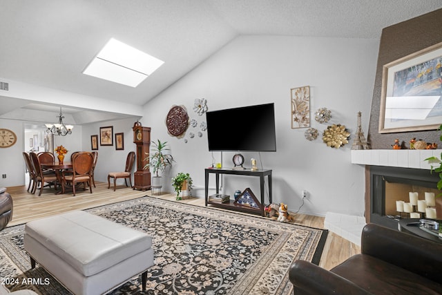 living area with visible vents, a notable chandelier, a fireplace with raised hearth, wood finished floors, and vaulted ceiling with skylight