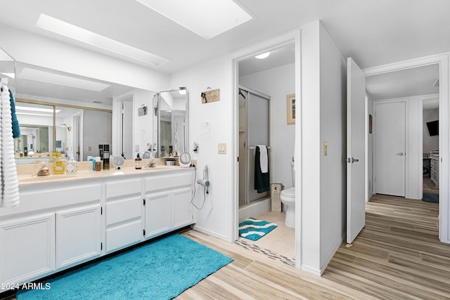 bathroom with vanity, wood finished floors, a skylight, a stall shower, and toilet