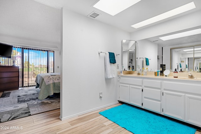 full bathroom with visible vents, double vanity, a skylight, ensuite bathroom, and wood finished floors