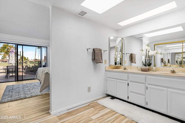 ensuite bathroom featuring a skylight, wood finished floors, double vanity, and a sink