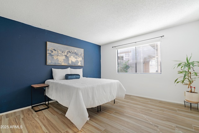 bedroom with a textured ceiling, wood finished floors, and baseboards