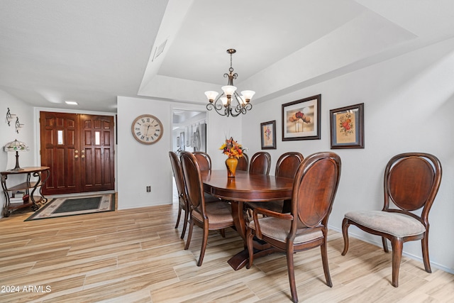 dining area with visible vents, a tray ceiling, an inviting chandelier, and light wood finished floors