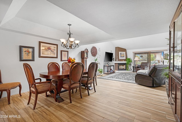 dining space featuring a textured ceiling, a fireplace, light wood finished floors, a chandelier, and vaulted ceiling