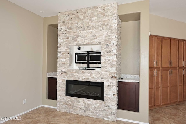 kitchen featuring light tile patterned floors, light countertops, brown cabinetry, and a fireplace