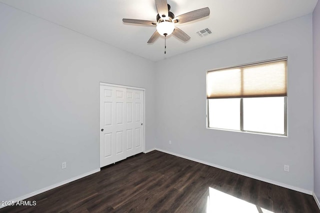 spare room with a ceiling fan, dark wood-style flooring, visible vents, and baseboards