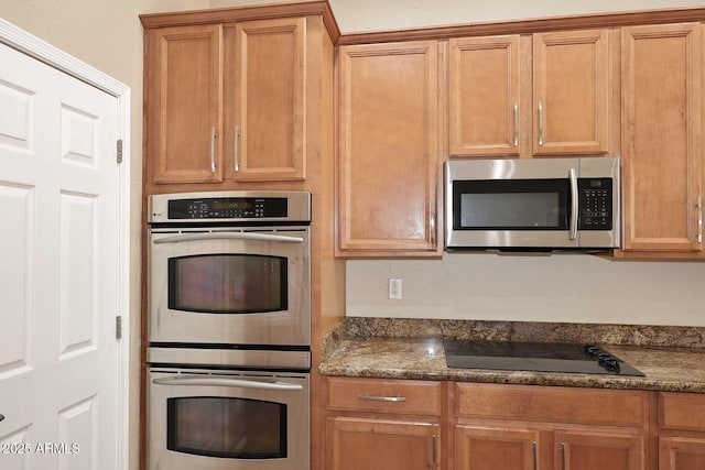 kitchen featuring appliances with stainless steel finishes, brown cabinets, and dark stone counters