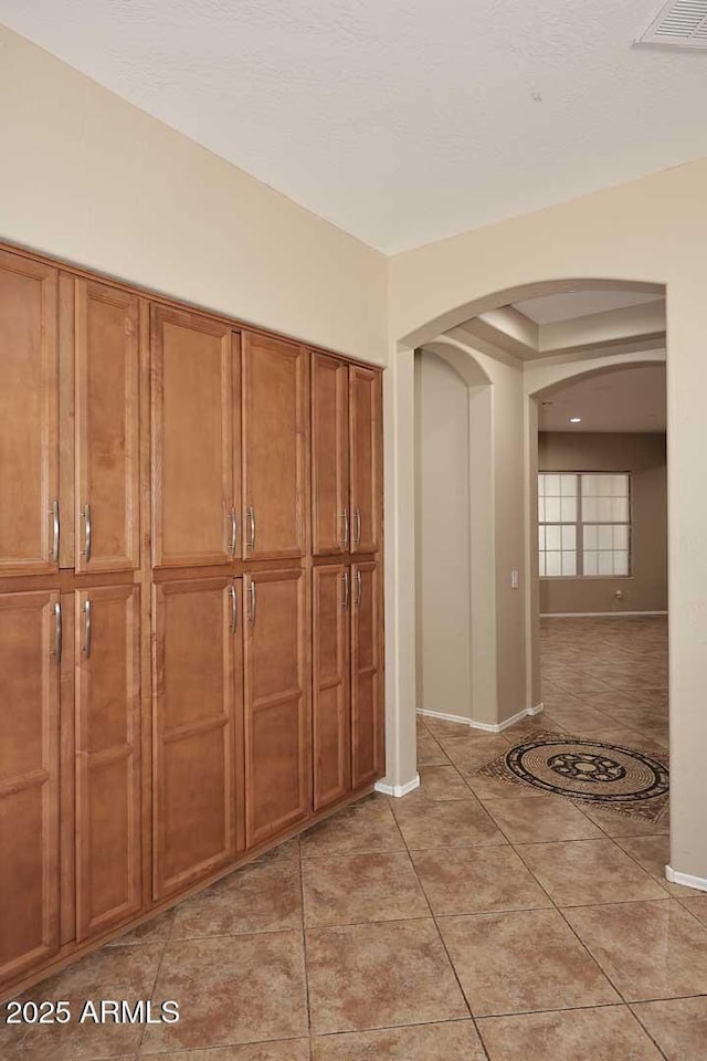 corridor with arched walkways, visible vents, baseboards, and light tile patterned floors