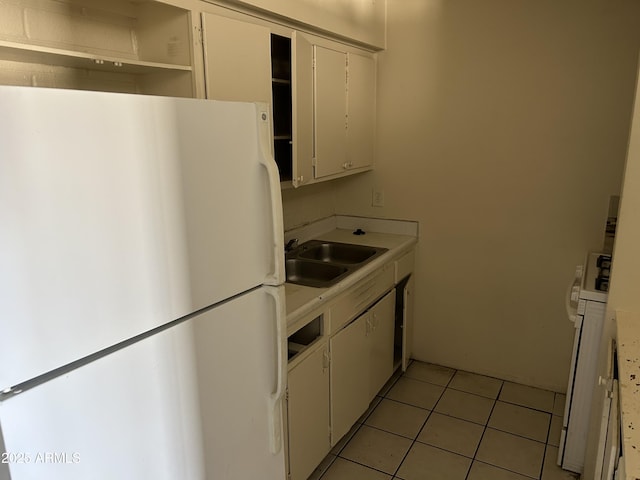 kitchen featuring light countertops, light tile patterned floors, freestanding refrigerator, white cabinets, and a sink